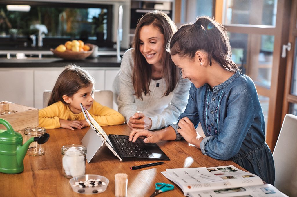 Woman sitting at table with two little girls working on a PC.