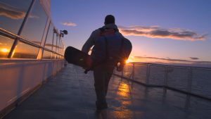 Still of an HDR video showing a man with a a snowboard and a backpack walking toward a sunset