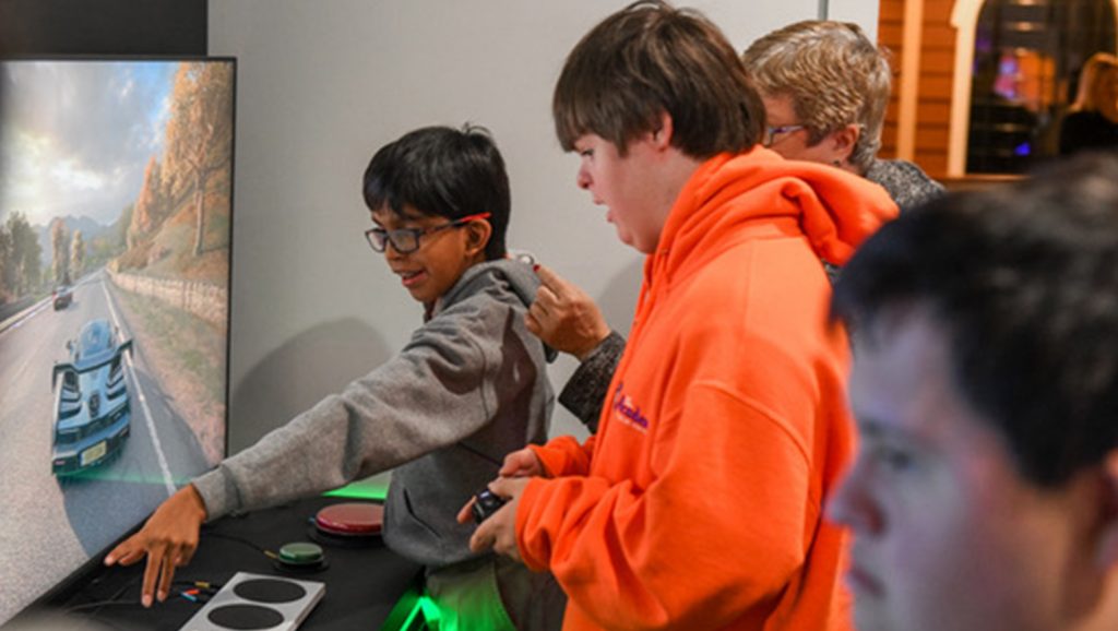 Three boys in front of a TV screen, playing a video game using the Xbox Adaptive Controller