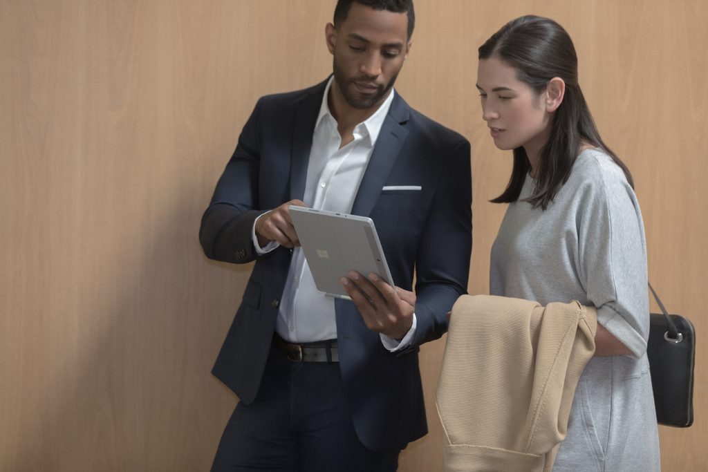 Man in business suit showing something on Surface Go screen to woman