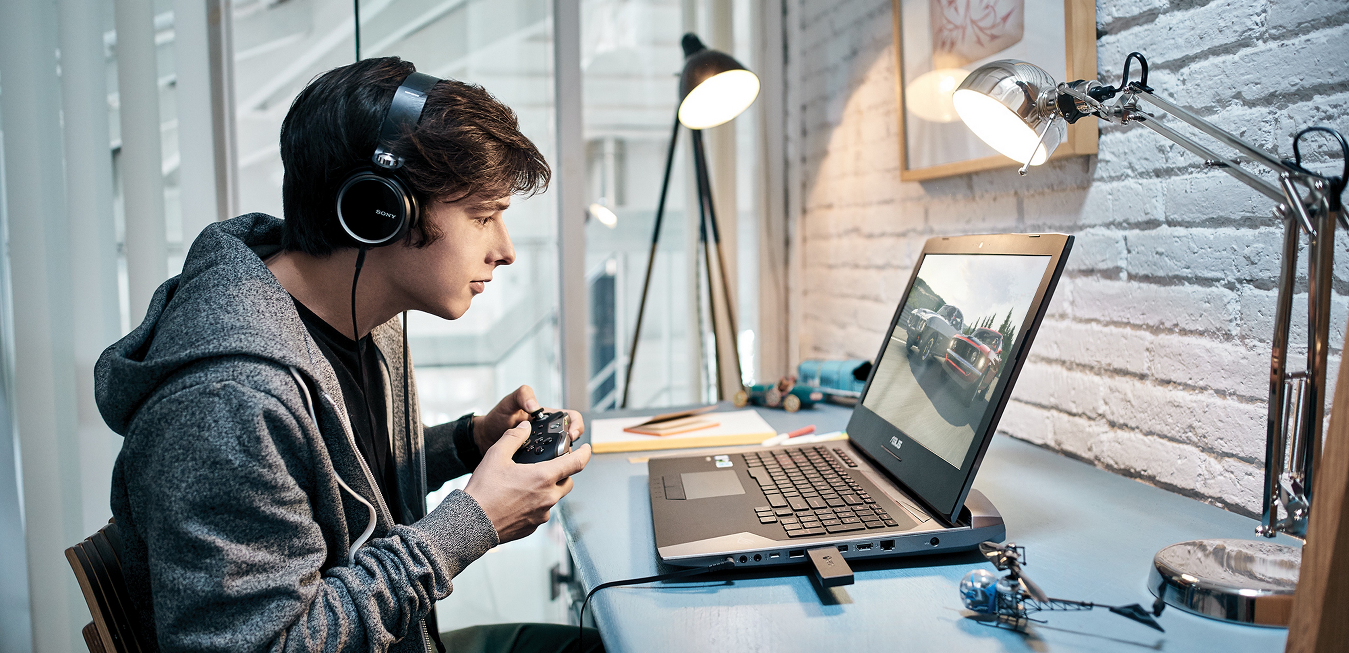 Young man sitting at a desk with headphones on plays video games on a Windows 10 PC with an Xbox controller.