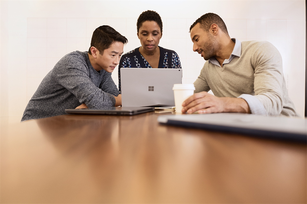 Three adults sitting at a table working together and looking at a Microsoft Surface Book.