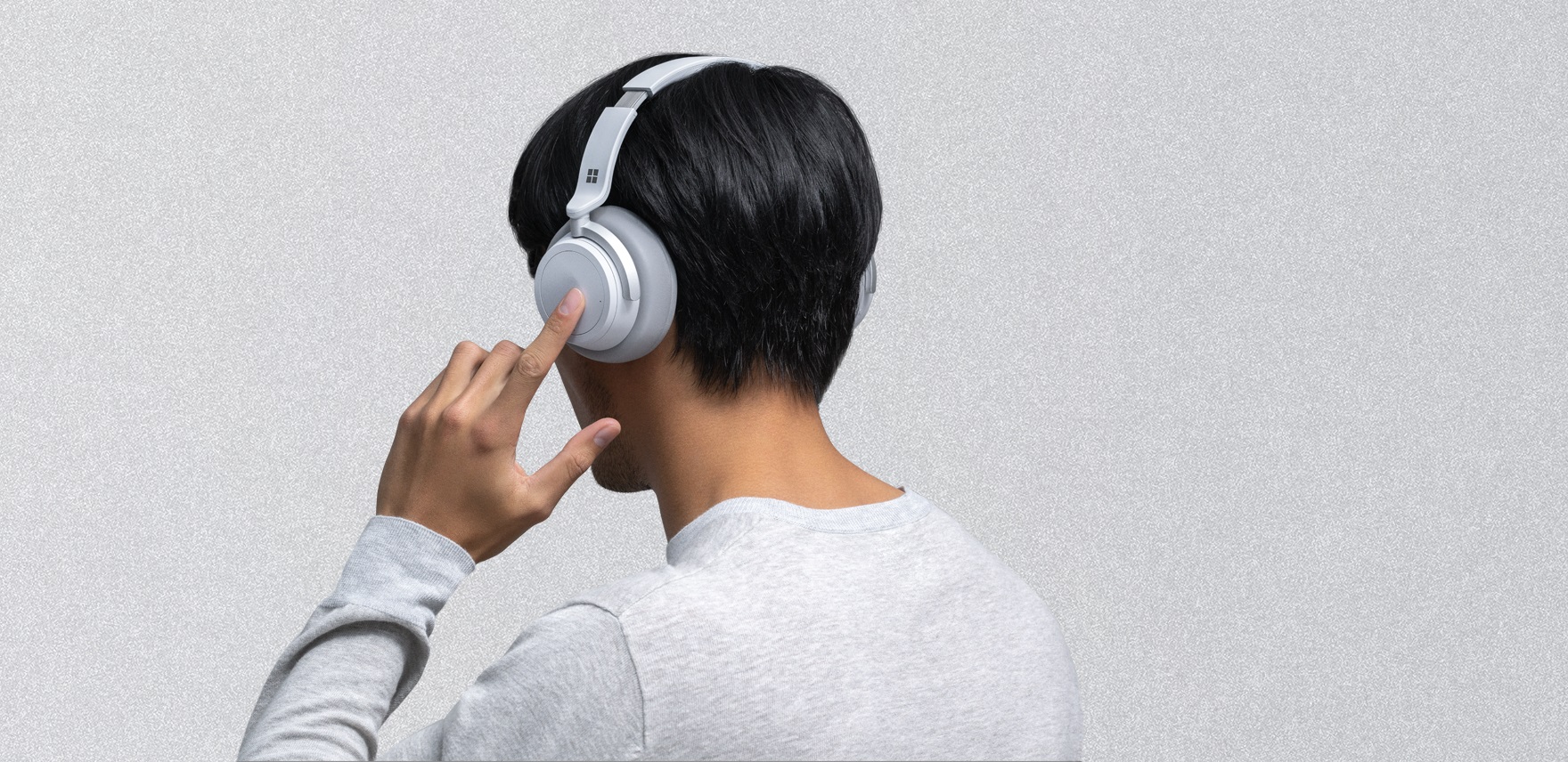 Photo of a man wearing Surface Headphones, touching the left earpiece