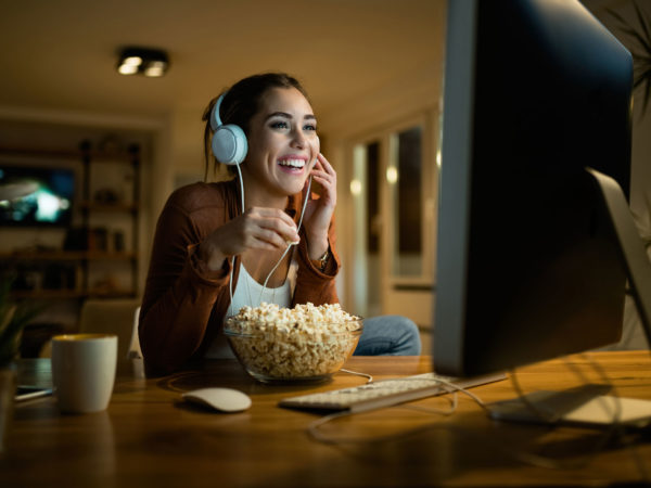 Woman wearing headphones eating popcorn while viewing a movie on her computer screen