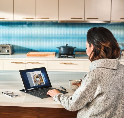 Женщина на кухе работает за ноутбуком
