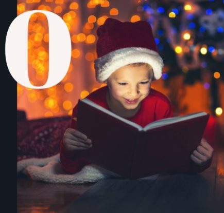 мальчик в колпаке новогоднего гномика читает вечером книгу в комнате с наряжнной елкой