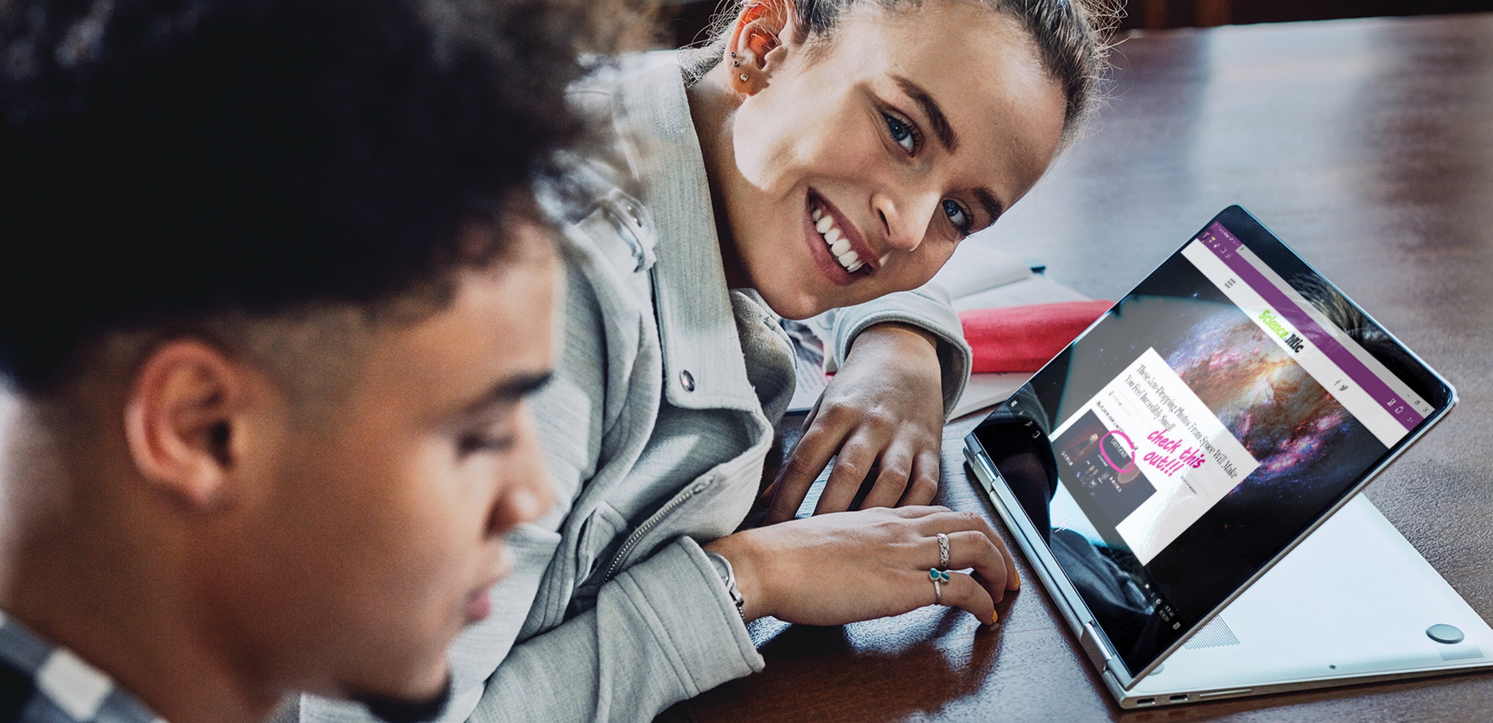 Man sitting next to a woman sitting at a desk smiling at the camera with an HP Windows 10 laptop in front of her where Windows Ink is being shown on the screen.