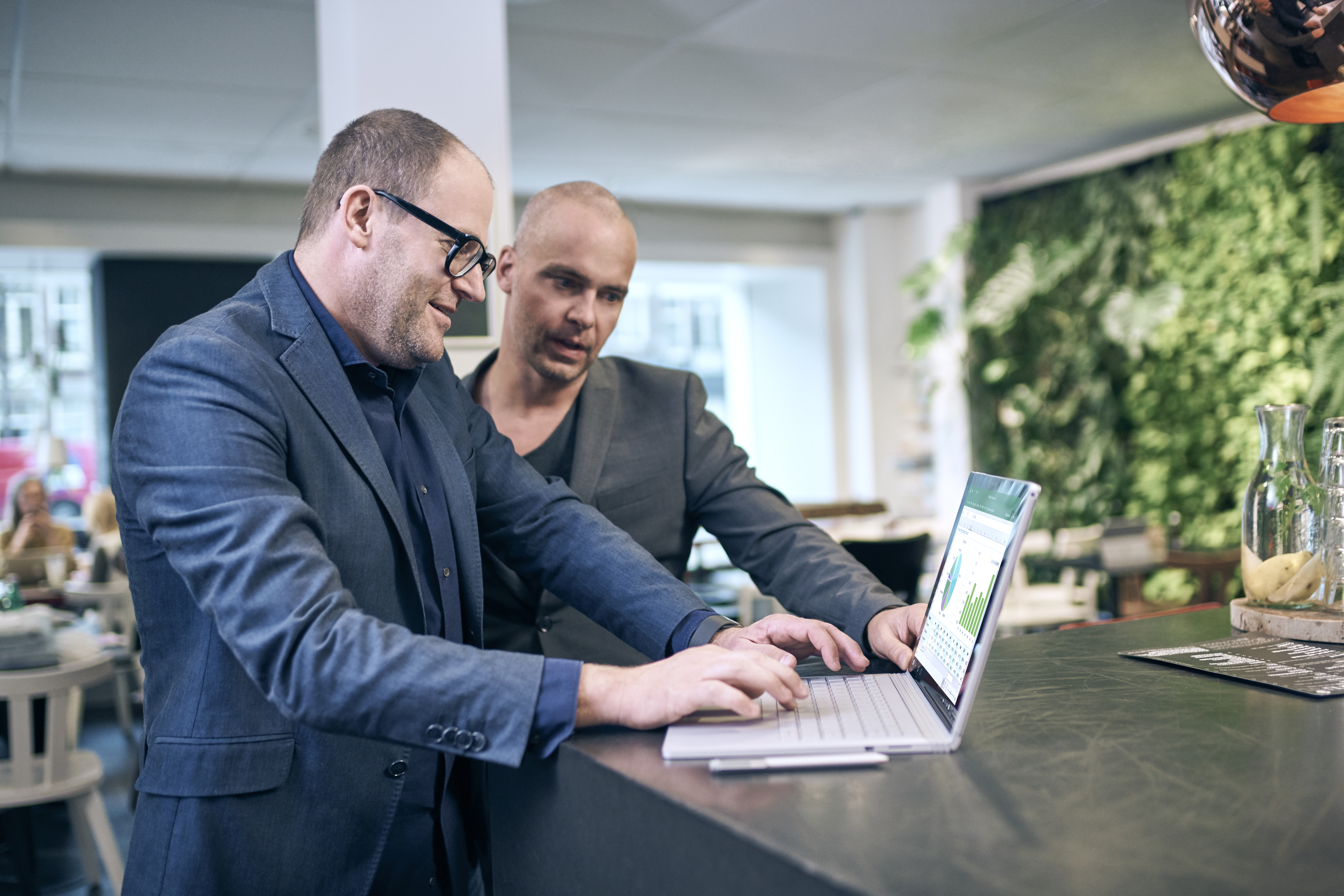 Two men in an office standing at a desk working on a Surface Book.