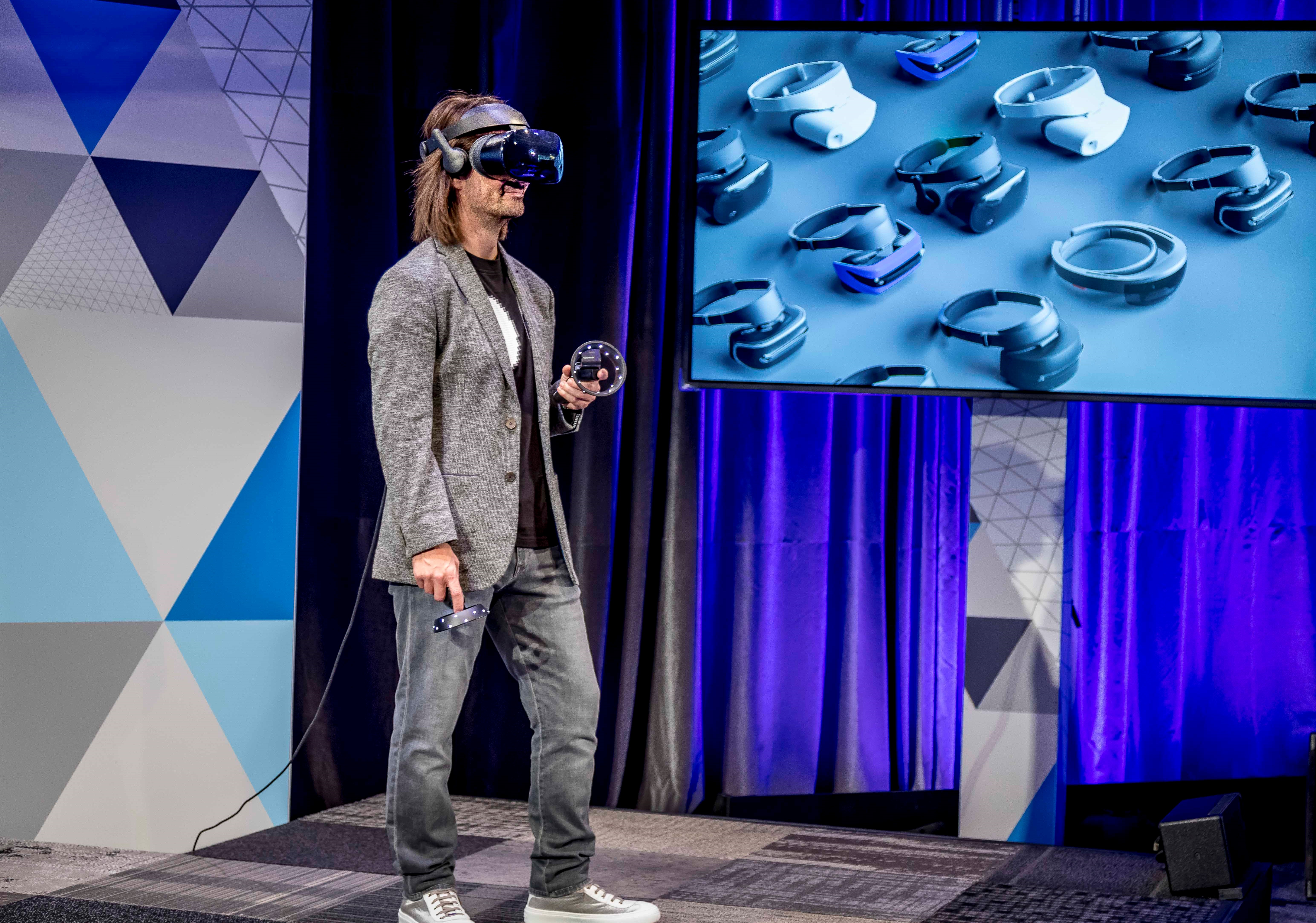 Alex Kipman standing on stage wearing the Samsung HMD Odyssey and holding motion controllers.
