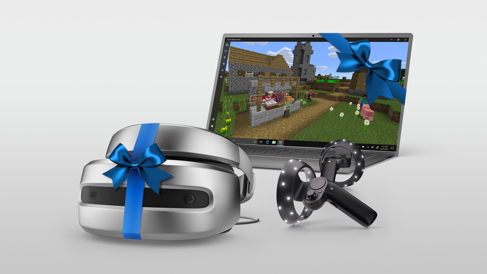 Windows Mixed Reality headset wrapped in a blue bow pictured next to a Windows 10 PC and Motion Controllers.