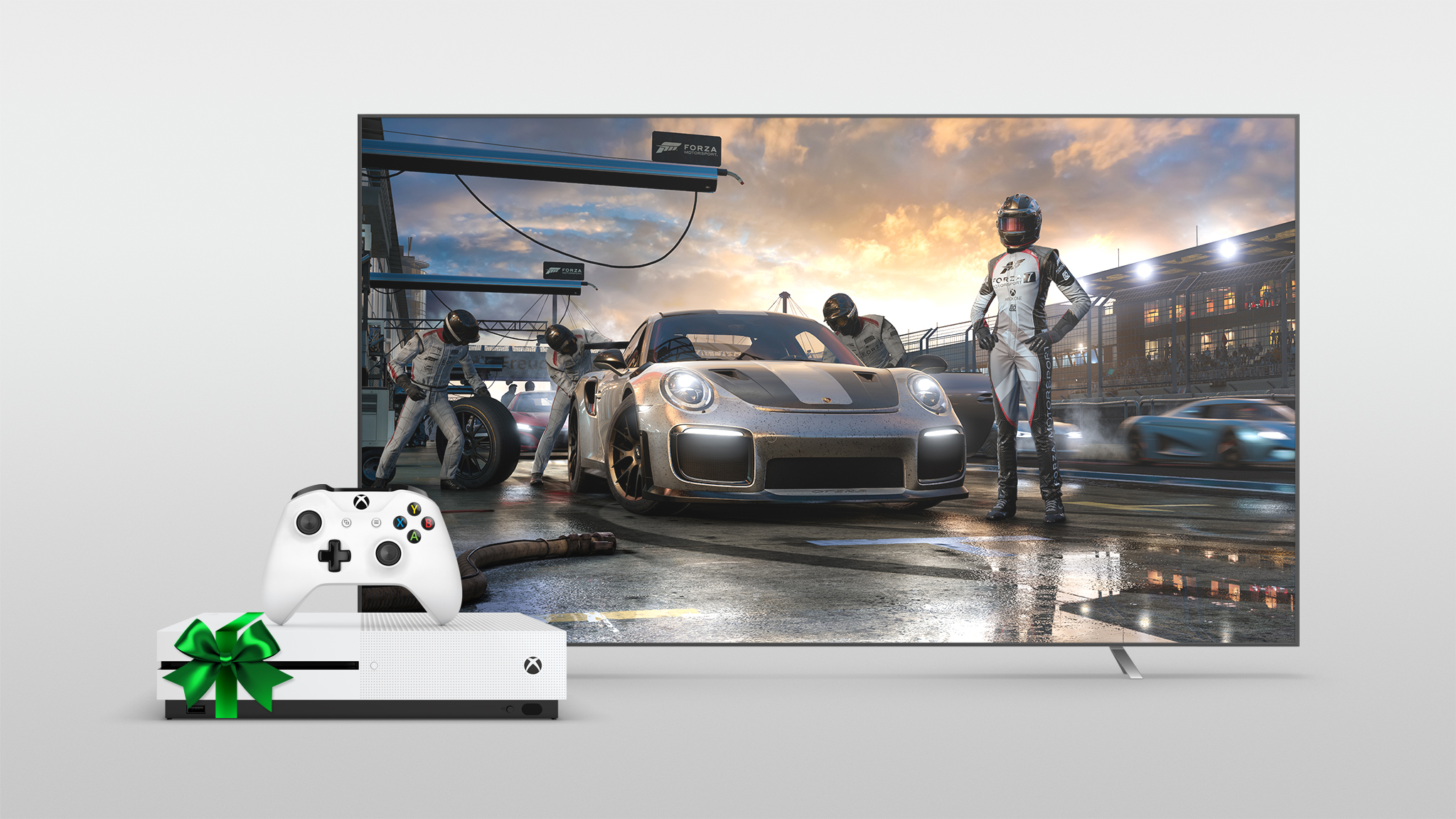 Xbox One S wrapped in a green bow next to a large TV with Forza shown on the screen