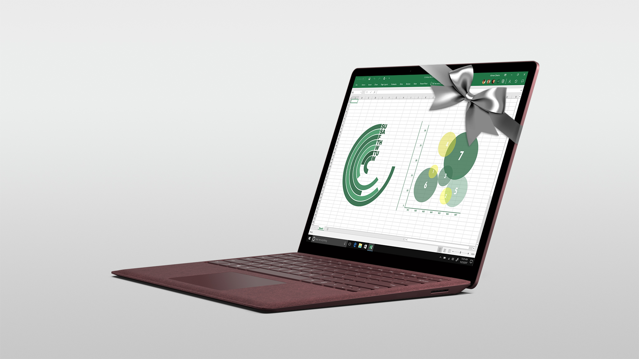 Surface Laptop in Burgundy wrapped in a silver bow with Excel shown on the screen.