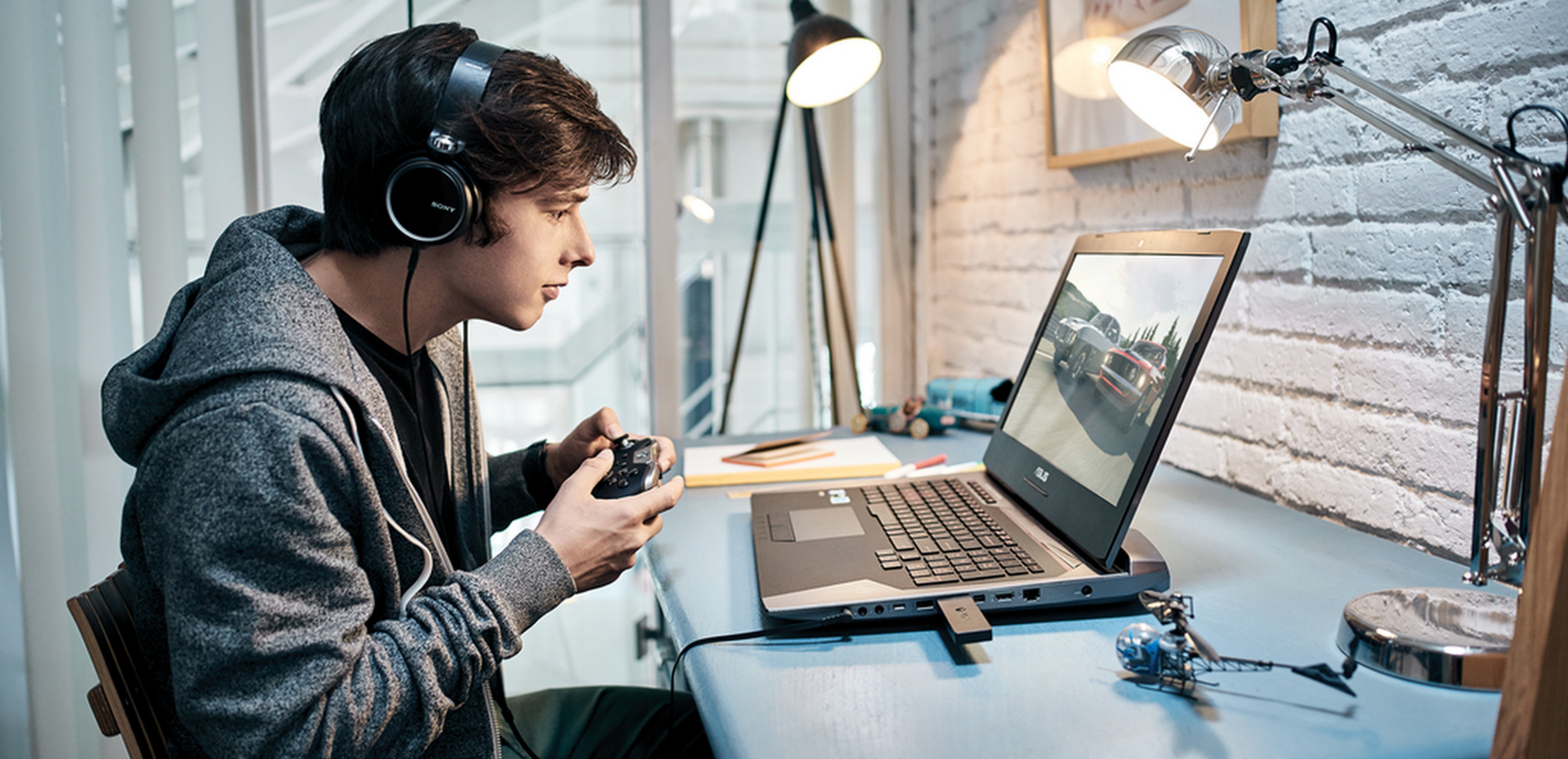 Boy sitting at a desk wearing headphones and holding an Xbox controller, gaming on a Windows 10 PC