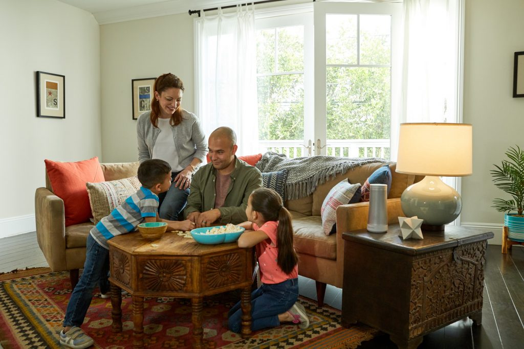 A family, two children, a mother and father sit around a table in a living room.