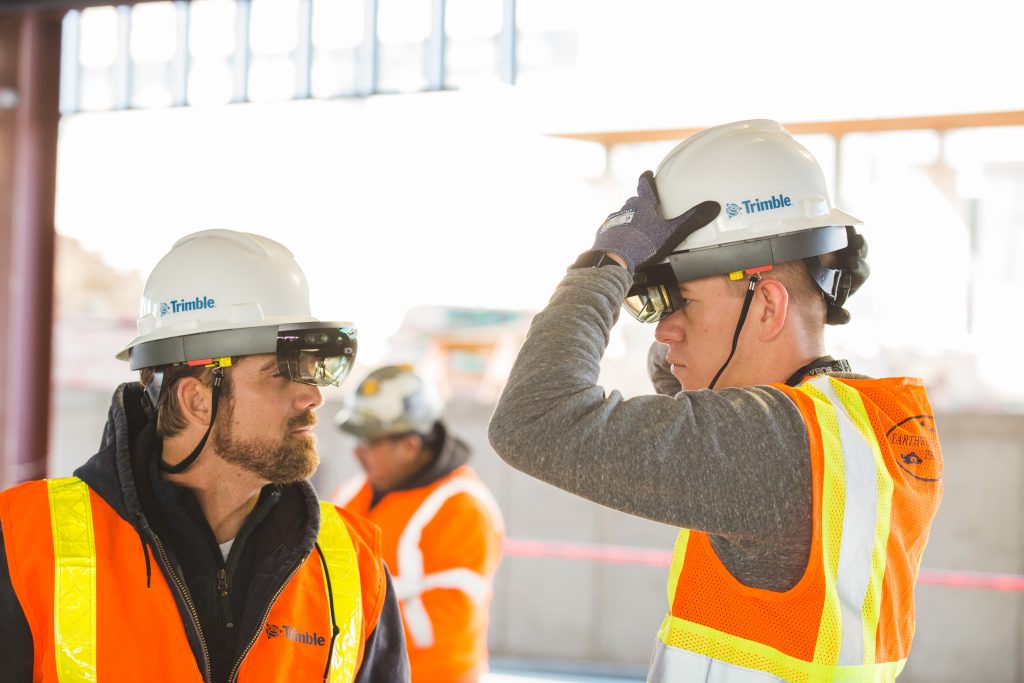 Two men wearing orange vests and hardhats with Microsoft HoloLens