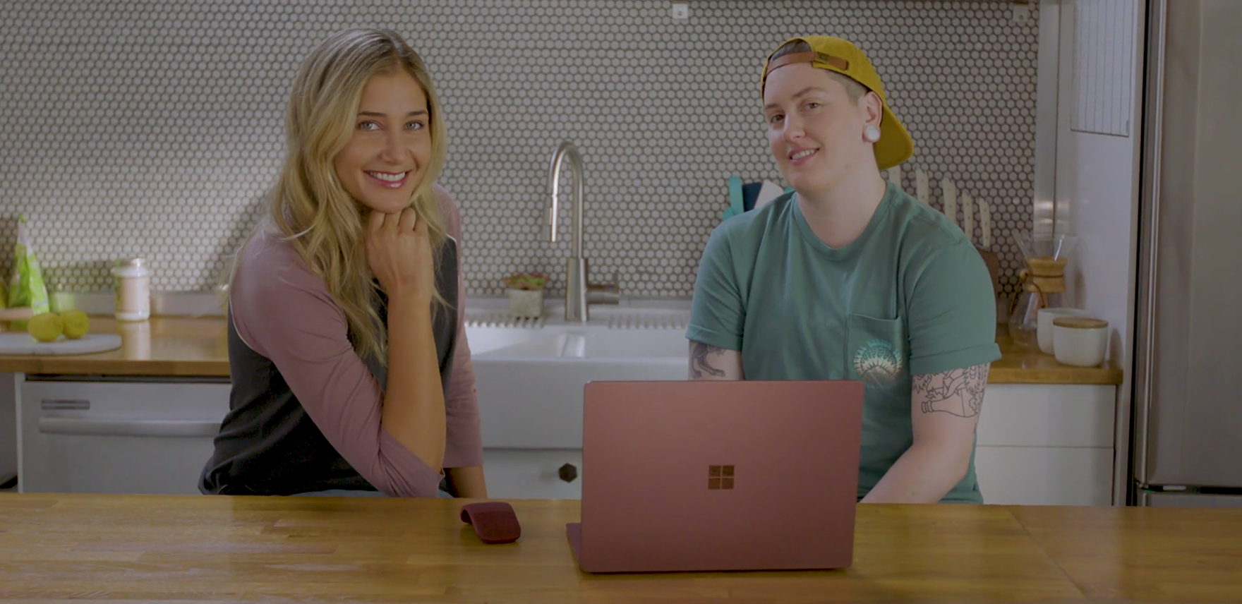 Alex Thomopoulos and Ashlie Little sit in a kitchen in front of a Microsoft Surface