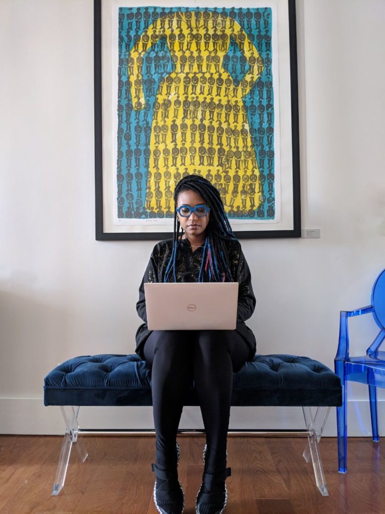 Photo of Rakia Reynolds sitting on a blue bench, working on a Dell laptop