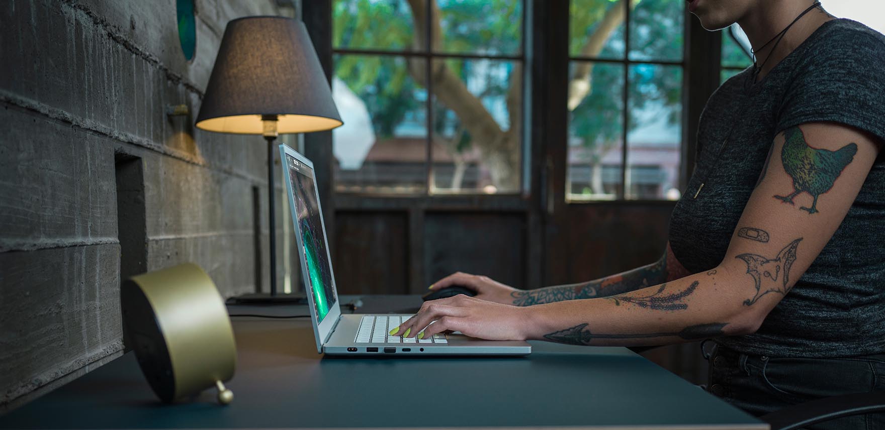 Person with a tattoo sitting at a desk working on a Razer Blade 15 Studio Edition laptop