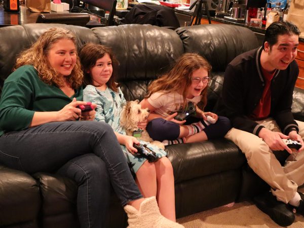 Woman on a couch playing video games with her two daughters, her husband and dog