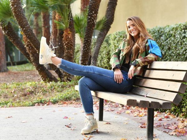 Sabrina Ionescu sitting on a bench in casual clothes with one leg outstretched