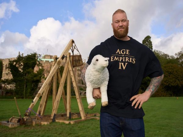 Man holding plushie sheep in front of a medieval catapult