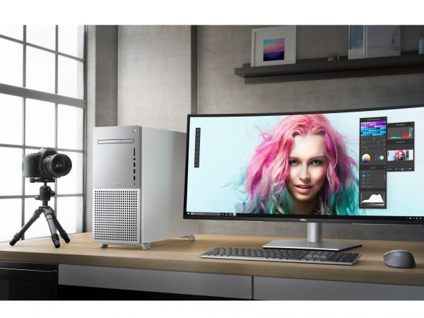 White Dell XPS Desktop on a desk with a woman with pink hair on monitor, next to a camera on a tripod