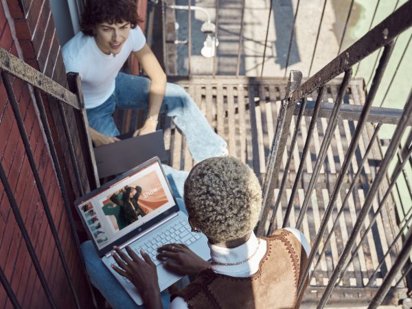 Two people sitting on a fire escape with one typing on a Windows 11 PC