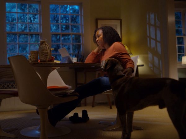 Woman at home petting her dog as she looks at her laptop computer