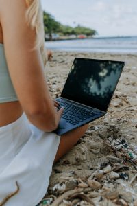 Woman on beach working on Lenovo laptop, as seen from behind