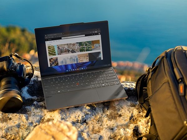 Laptop sitting on a cliff ledge next to a camera and backpack, with water in the background