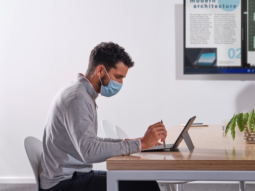 Man wearing a mask working on a laptop computer