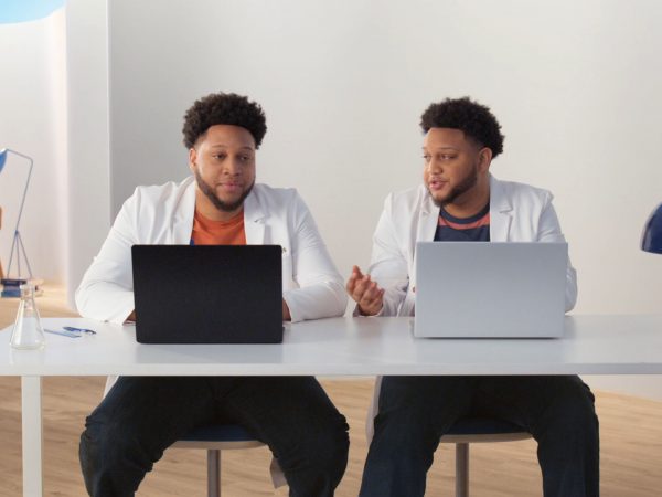 Two men in lab coats sitting at a desk in front of PC laptops