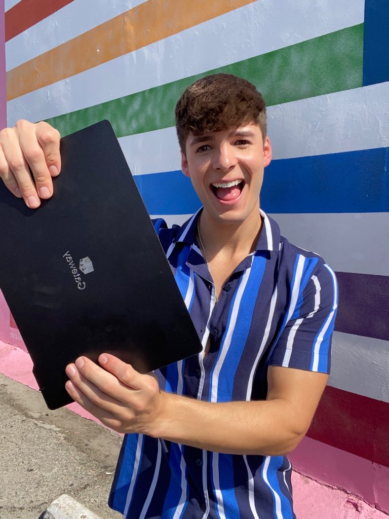 Man smiling and holding a closed black Gateway laptop