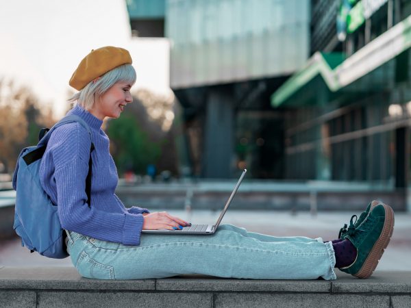 Woman sitting outside with legs outstretched, working on laptop on her legs