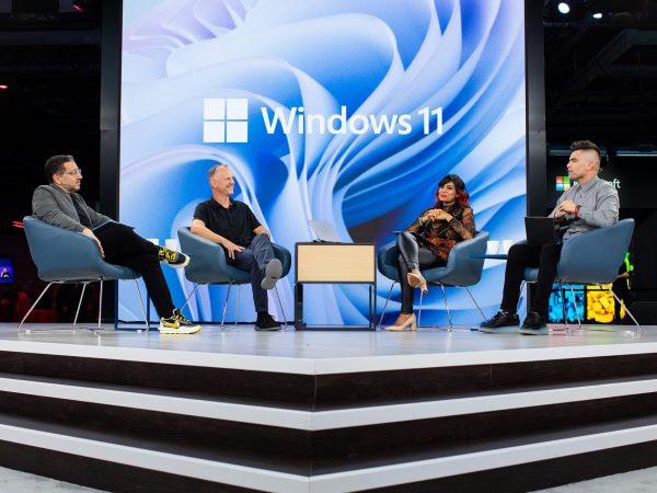 Four people seated on stage with a Windows 11 logo as the backdrop