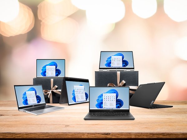 6 Windows 11 laptops open and spread out over a table with blurred lights in the background