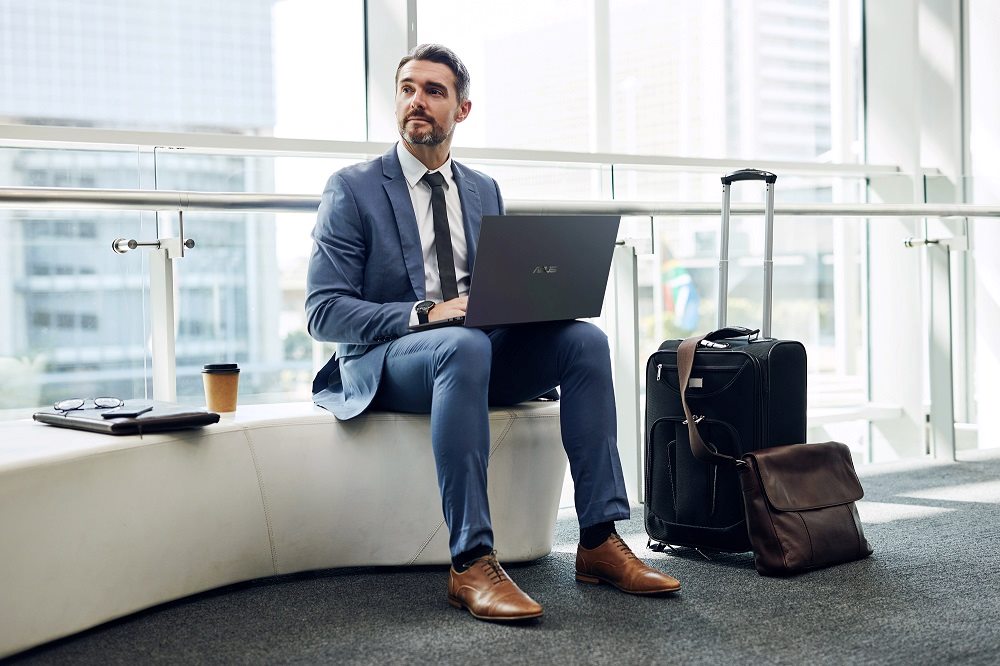Man in a suit sitting next to a suitcase, working on a laptop