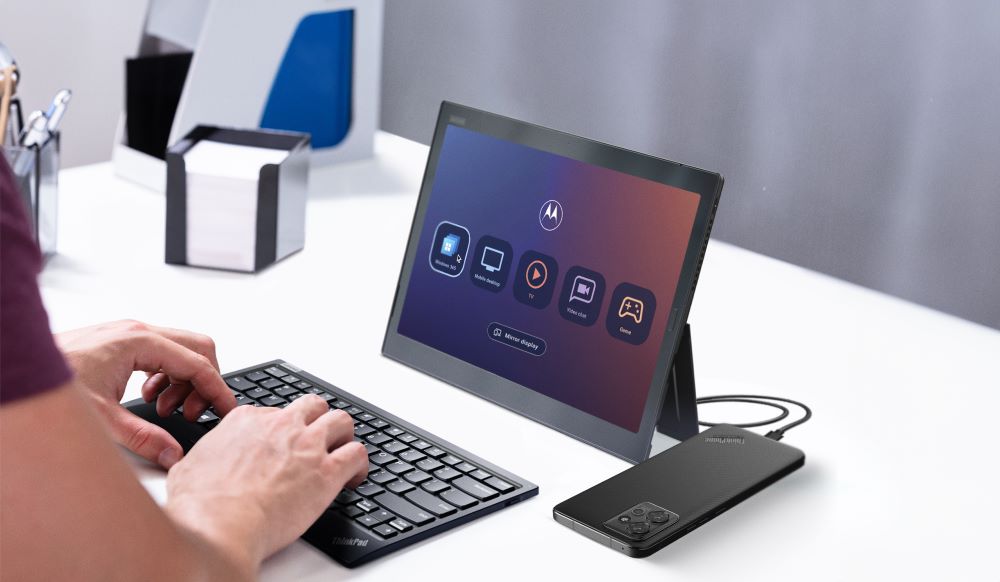 Person typing on keyboard with tablet upright and phone connected to it