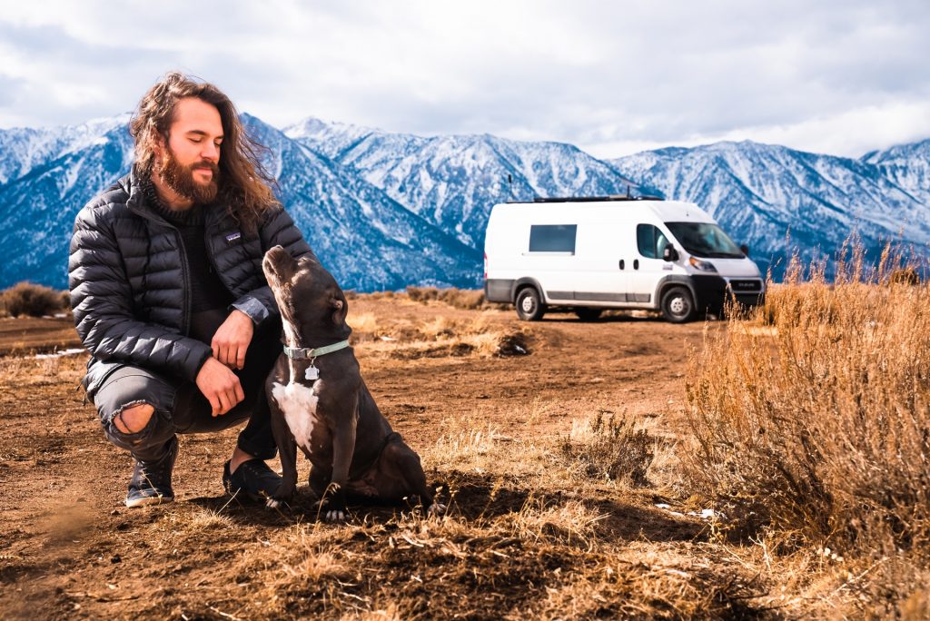 Man with dog with van and mountains in background