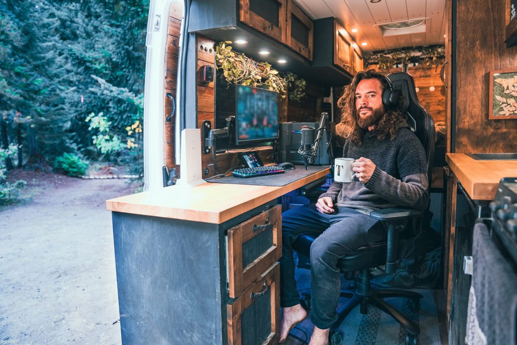 Man sitting in van holding a mug with door open showing forest outside
