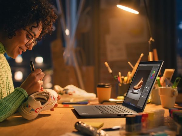 Woman painting sneaker looking over at laptop on work table