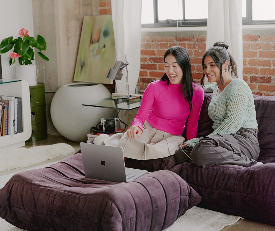 Two women sitting on a couch enjoying entertainment displayed on a laptop computer