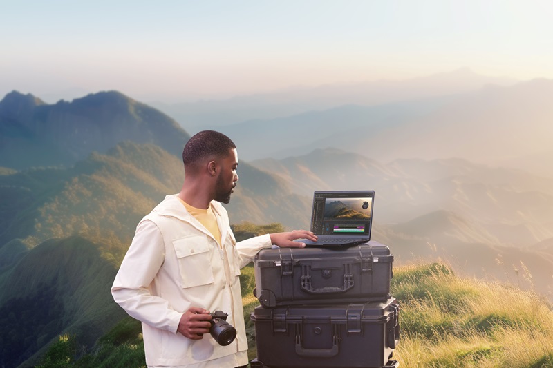 Man looking at laptop screen showing mountains in background