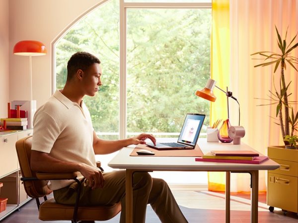 Man sitting in a sunlit room at a table working on a laptop