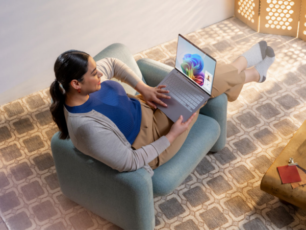 An adult using a Copilot+ PC while casually sitting sideways in a soft, blue accent chair