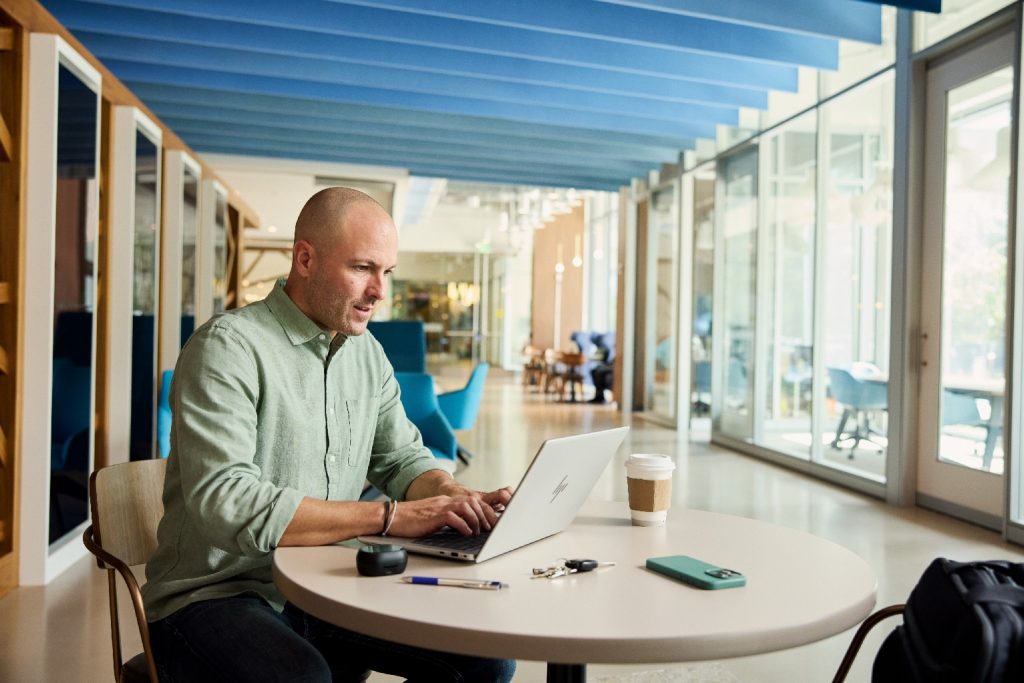 Man working on a laptop in a room with a wall of windows