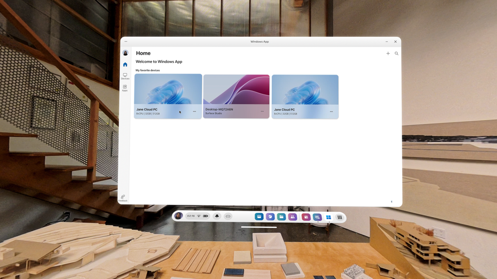 A mixed reality view of a workspace with architectural models on a wooden table in the foreground. A virtual window displays the Windows App interface, showing a home screen with three Cloud PCs. The Meta Horizon OS taskbar floats at the bottom of the view.