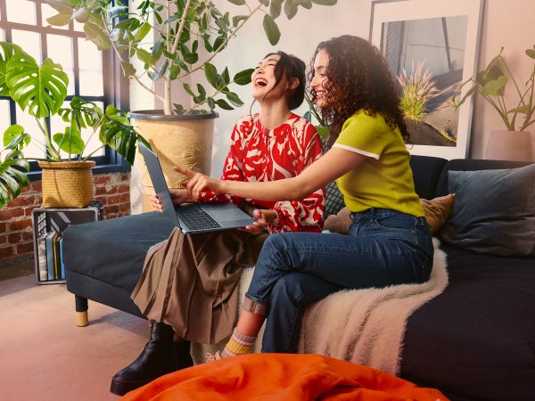 Two women sitting on a couch enjoying what they're watching on a laptop computer