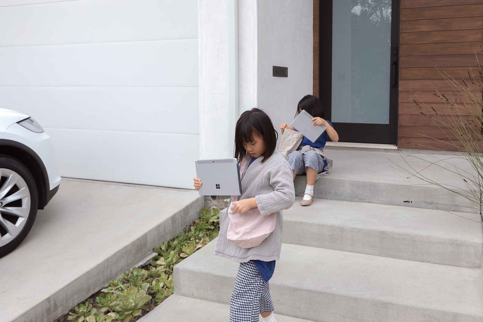バッグに Surface Go 2 を入れて家から出る子ども2人