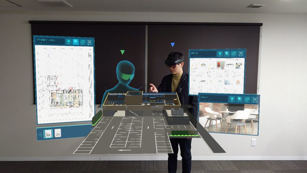 ホロストラクションのイメージ画像。中央に、HoloLens 2 を装着した人と、遠隔地にいるひとのアバターが表示されており、その周辺に３Dの建設モデルや、書類、画像データがホログラムとして表示されている。